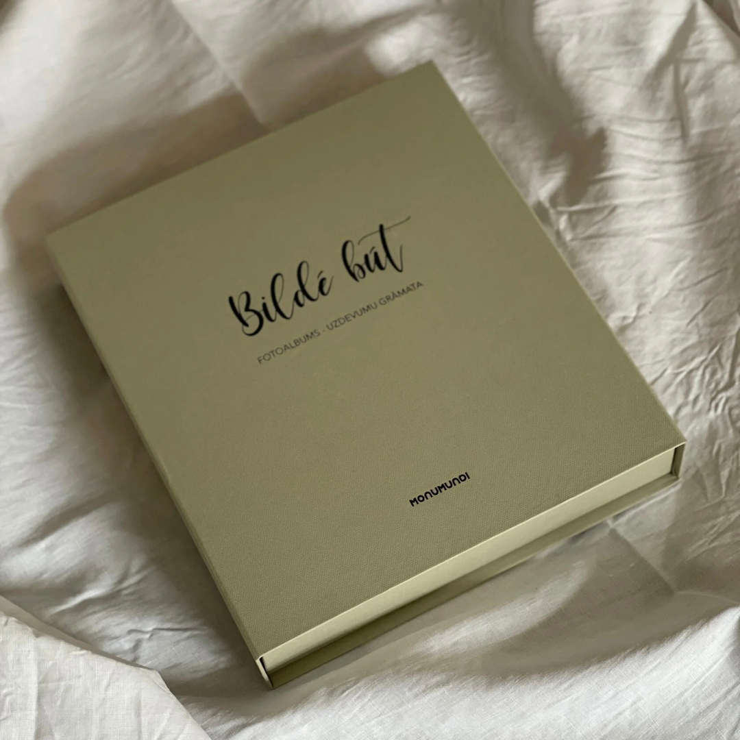Fotoalbums "Bildē būt" ar bēšu vāku un melnu vāka apdruku. Albumam ir magnētiska aizdare un melns metāla riņku mehānisms iekšlapu stiprināšanai.